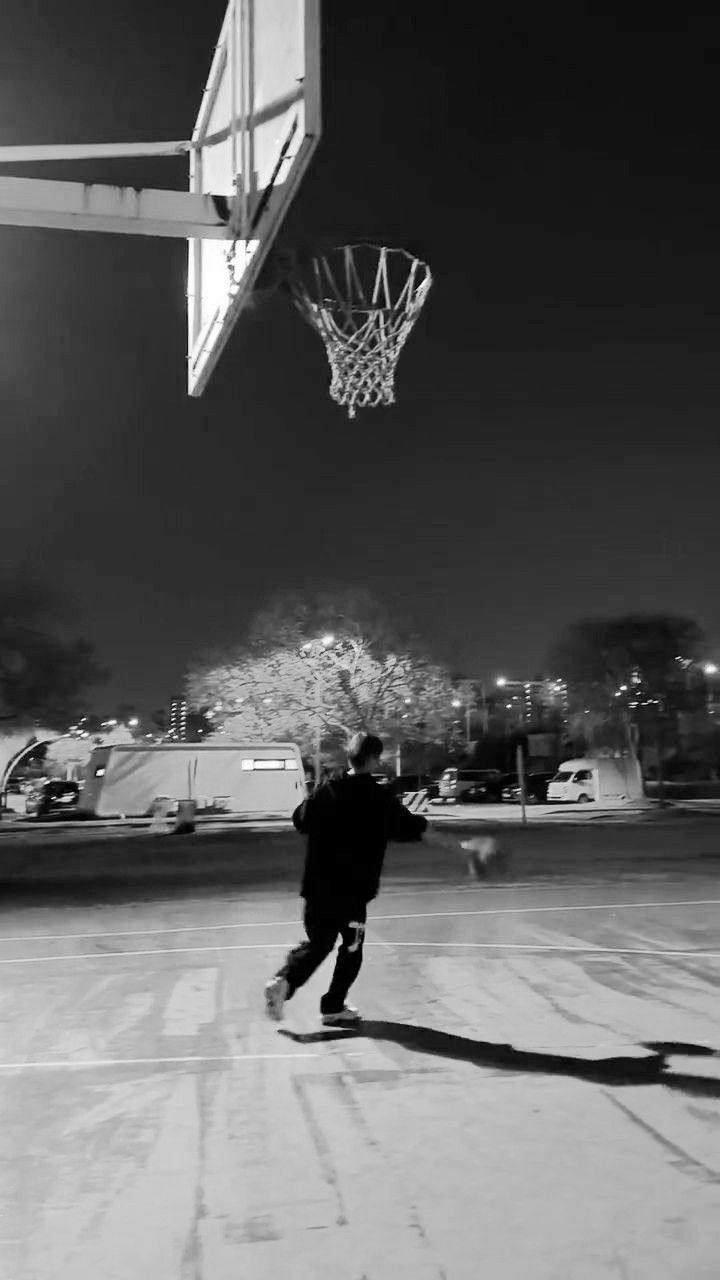 a young man is playing basketball on an empty parking lot at night with the lights turned on