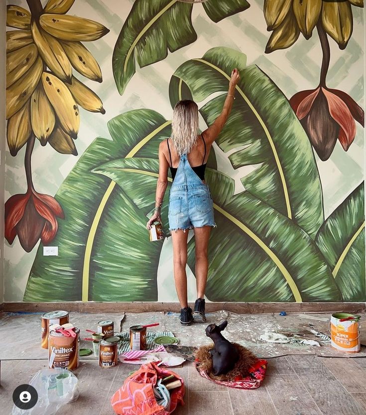 a woman standing in front of a painting on the wall with her hand up to paint it