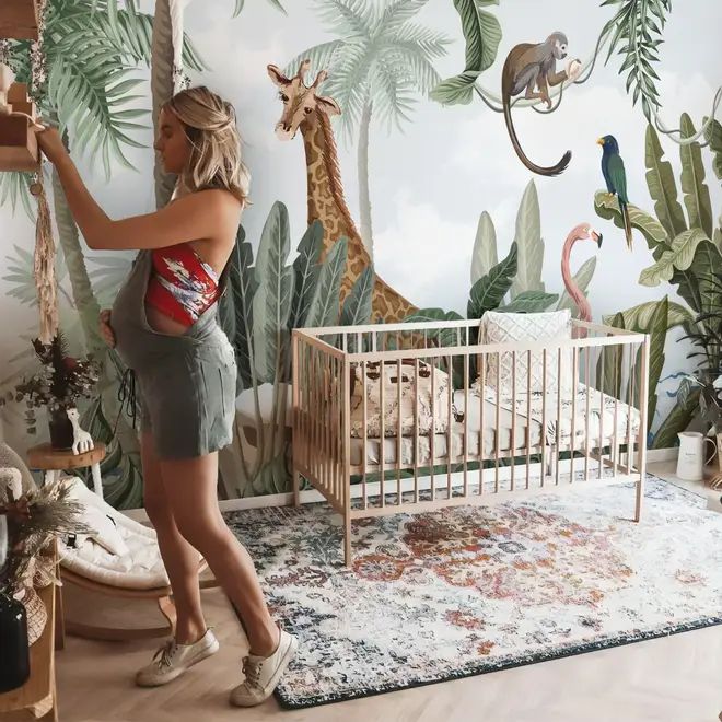 a woman standing next to a baby in a crib with giraffes on the wall