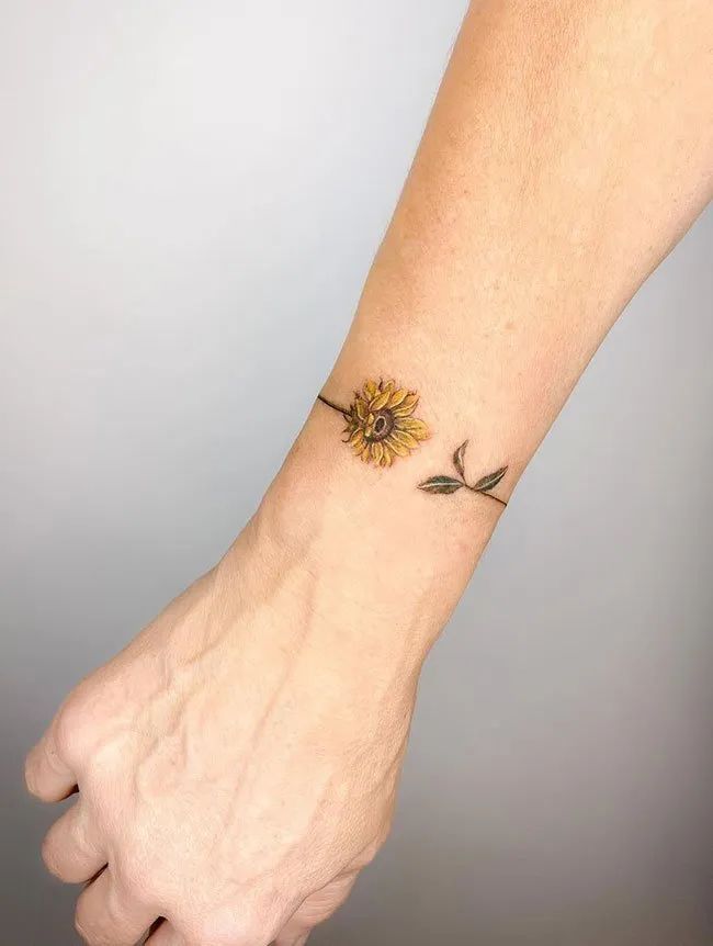 a sunflower tattoo on the wrist is shown in black and yellow colors with leaves