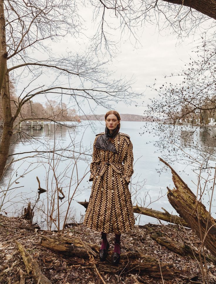 a woman standing in front of a body of water wearing a long dress and boots