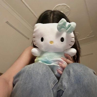 a girl holding a hello kitty stuffed animal in her lap and looking at the camera