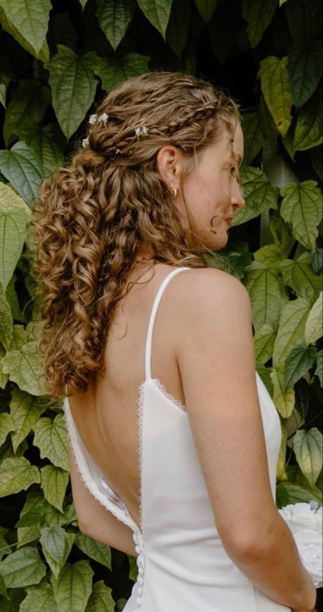 a woman wearing a white dress standing in front of some plants and greenery with her back turned to the camera