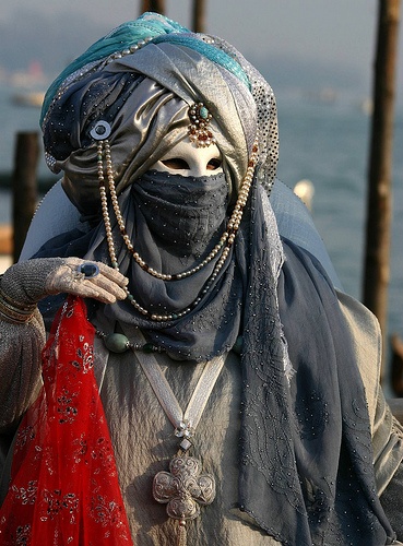 a person in costume standing next to the ocean with beads on their head and face