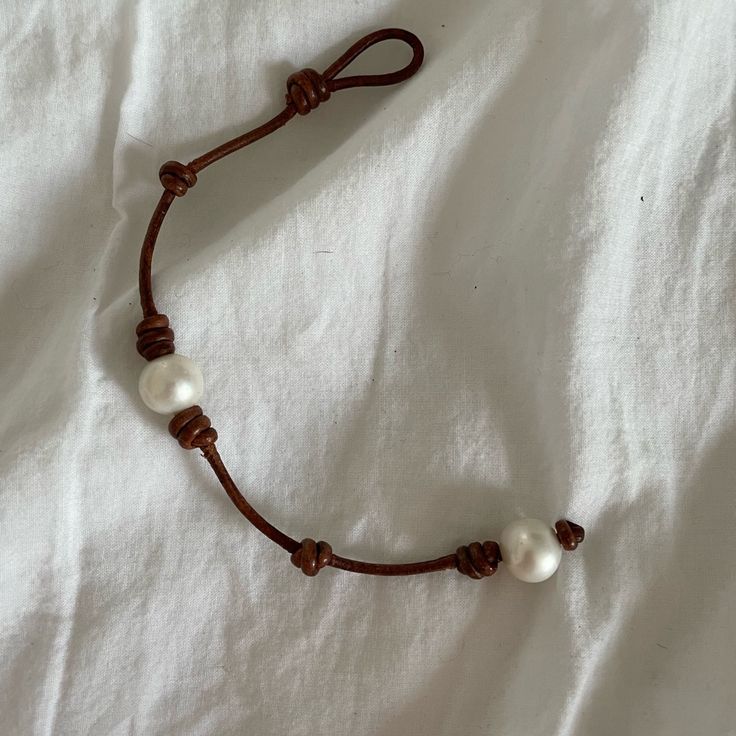 a brown string bracelet with two white pearls