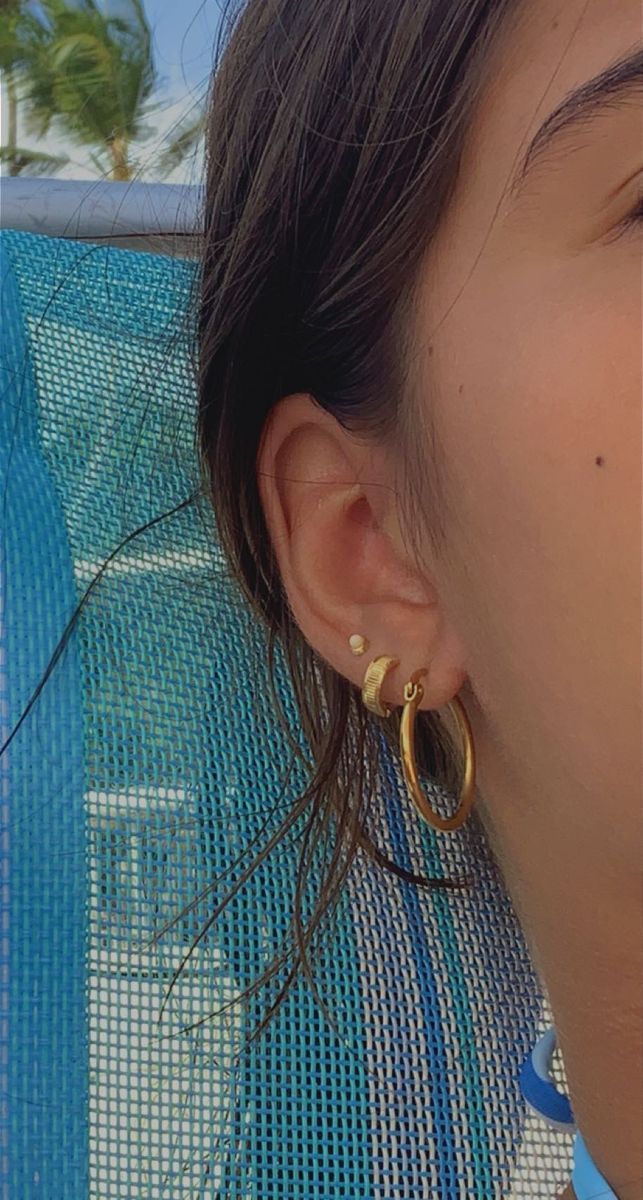 a close up of a person wearing large gold hoop earrings on their ear and looking off into the distance