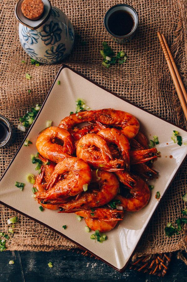 a white plate topped with cooked shrimp next to chopsticks and two cups of coffee