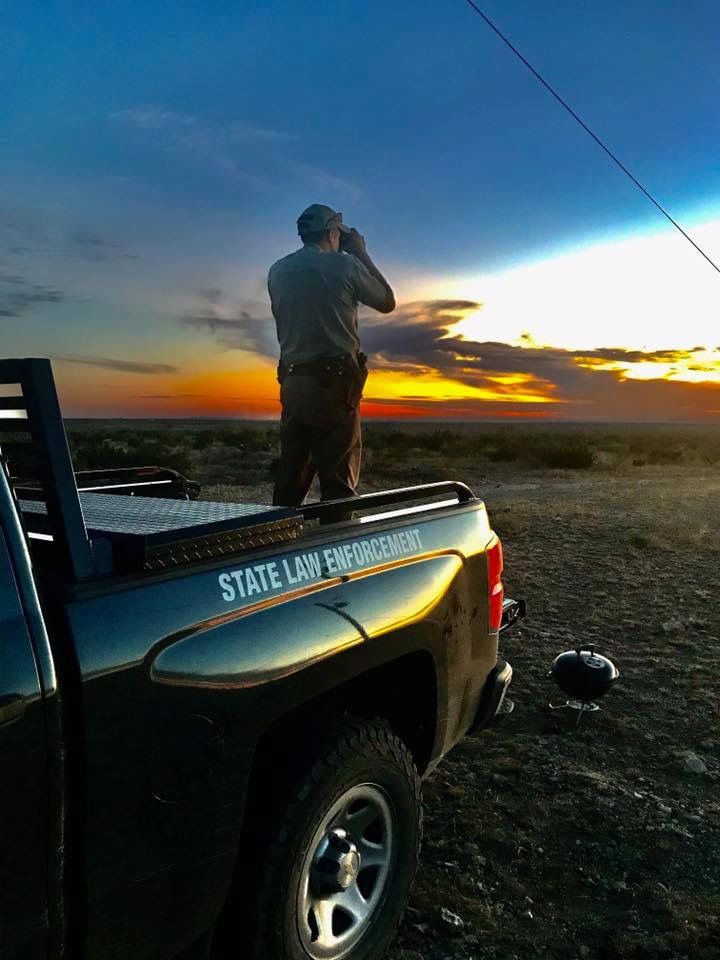 a man standing on the back of a truck talking on a cell phone at sunset