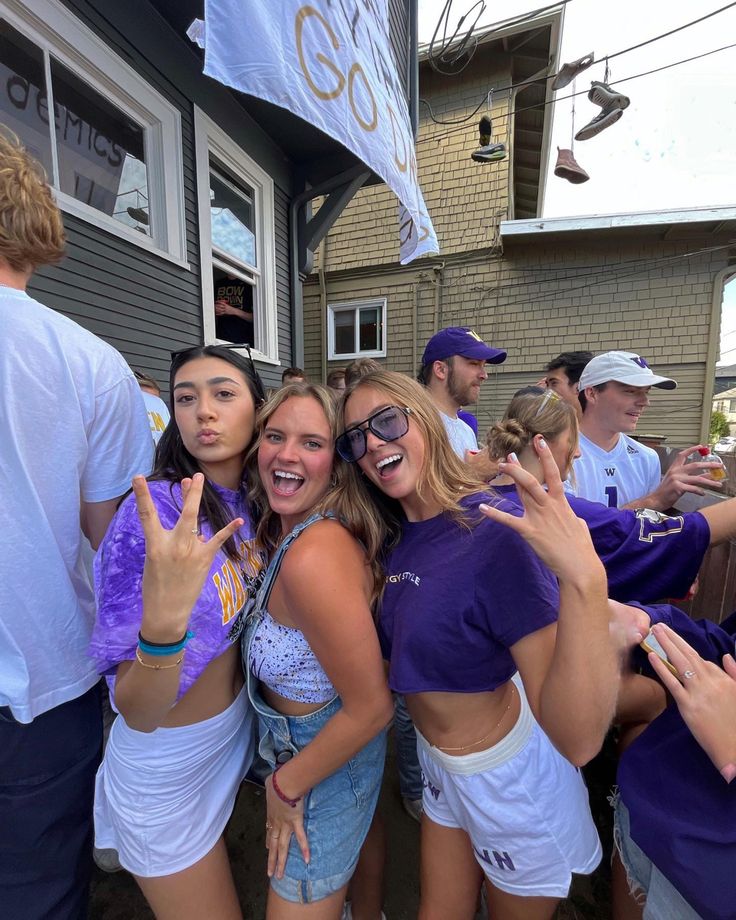 a group of young women standing next to each other in front of a house holding up their hands