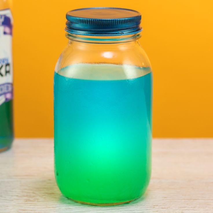 there is a blue and green liquid in a glass jar next to an orange bottle