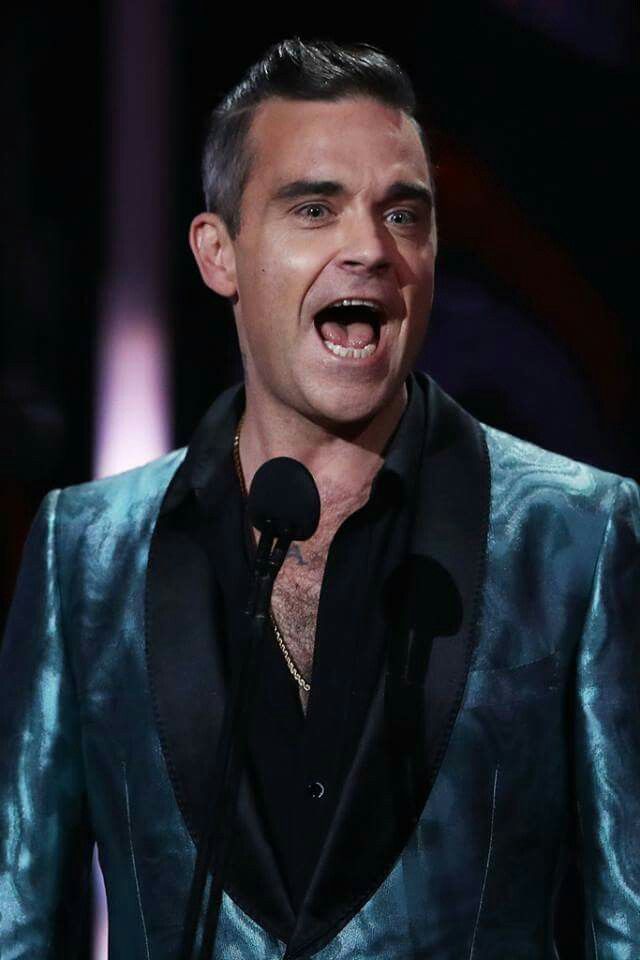 a man in a blue suit and black shirt with his mouth open while speaking into a microphone