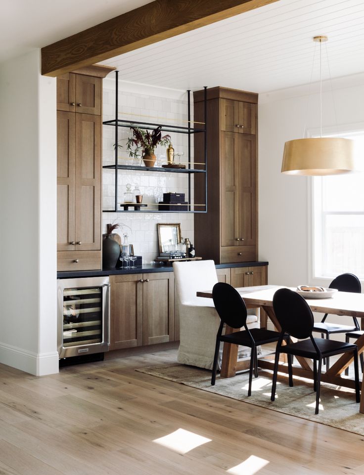 a dining room table and chairs in front of a kitchen with open cabinets on the wall