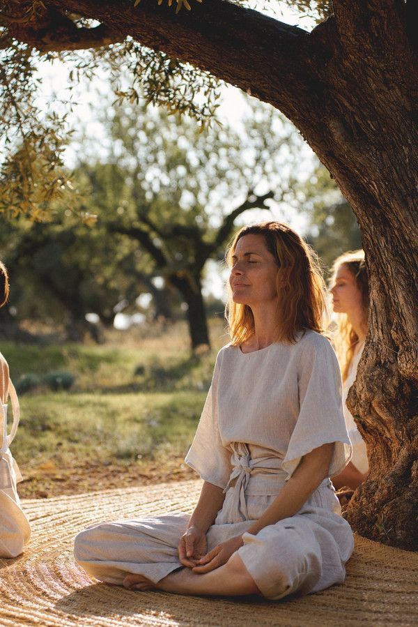 two women are sitting on the ground in front of a tree and one is meditating