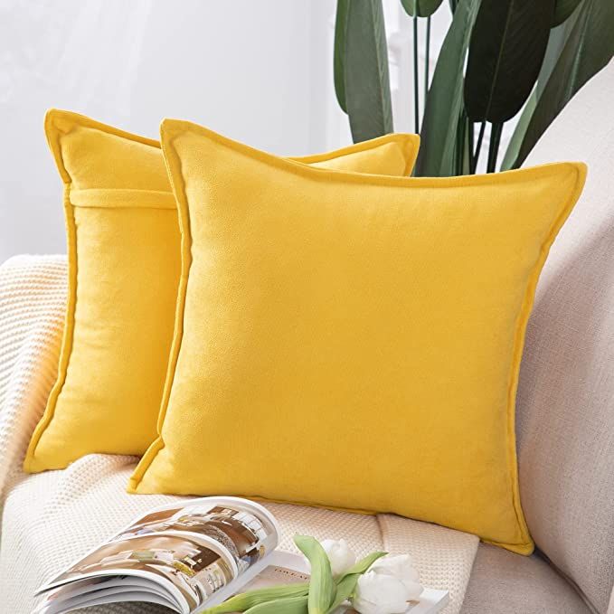 two yellow pillows sitting on top of a white couch next to a vase with flowers