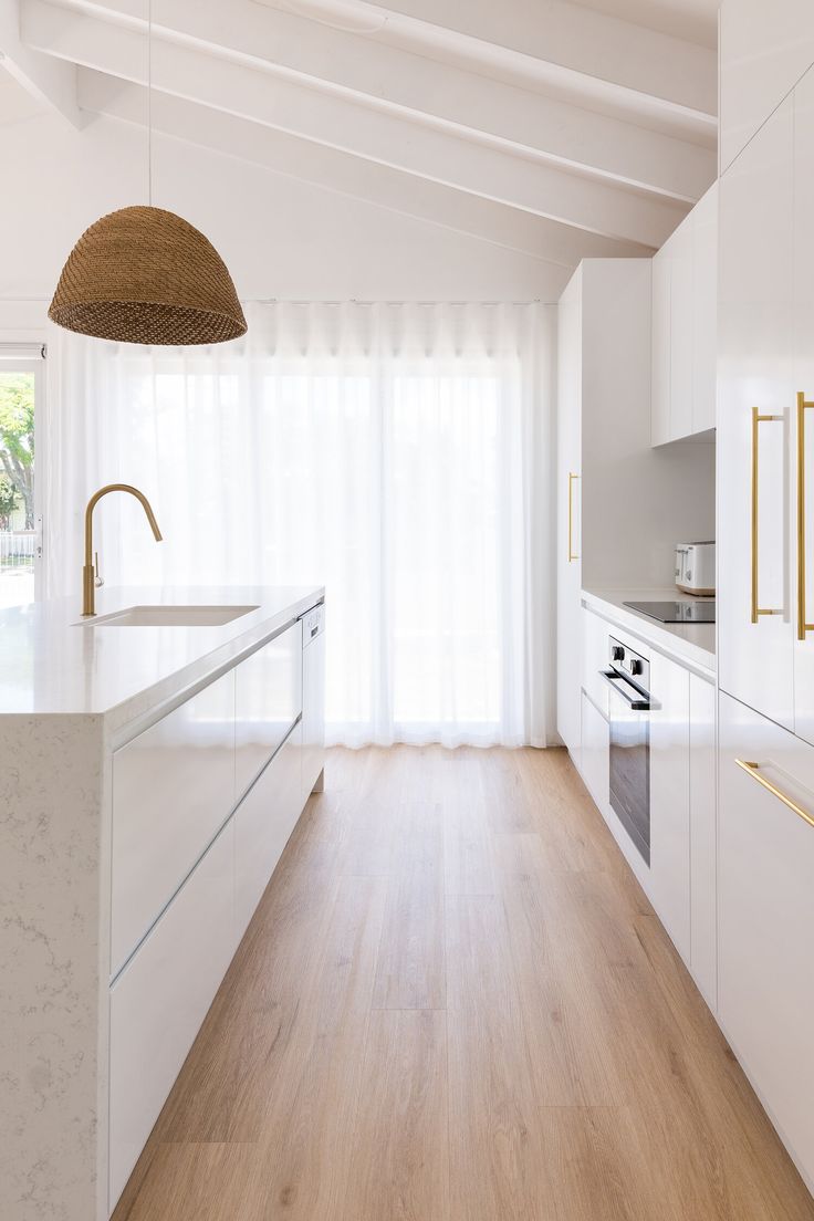 a kitchen with white cabinets and wood flooring next to a large window that looks out onto the backyard