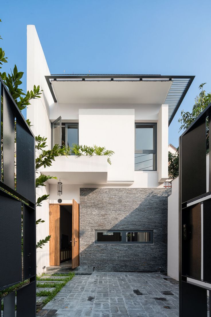 an entrance to a modern house with black and white doors, brick walkway and green trees