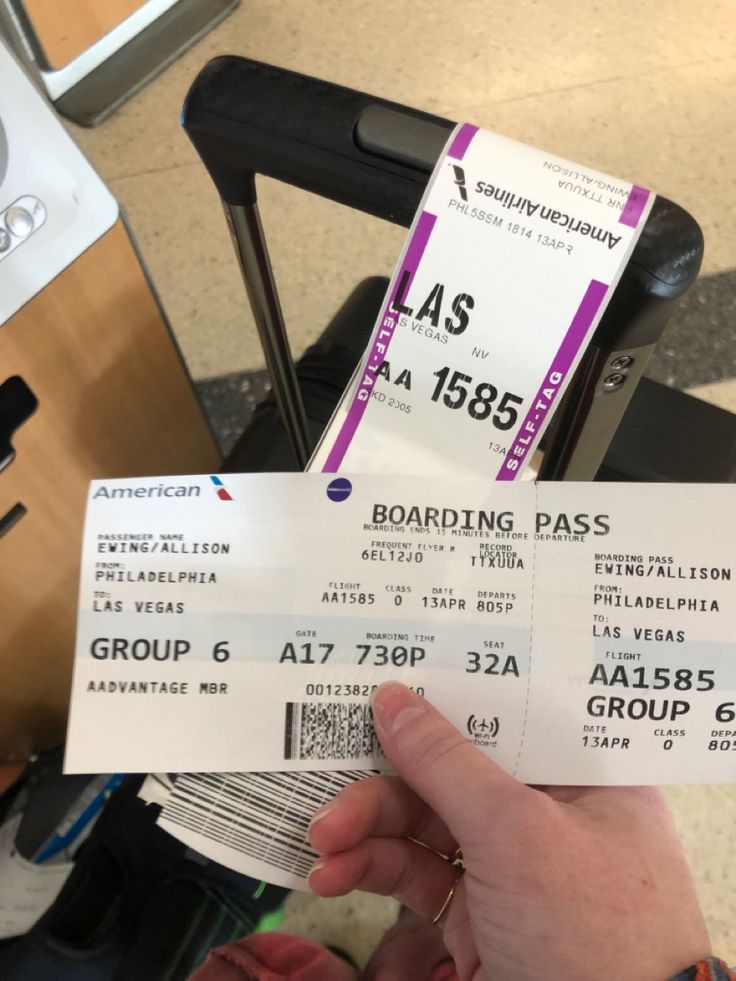 two tickets are held up in front of a person's hand at an airport