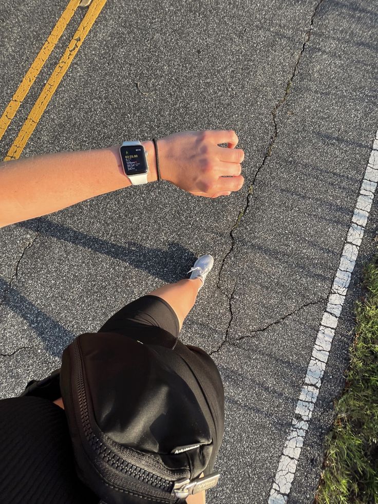 a person wearing a watch on their wrist sitting in the middle of an asphalt road