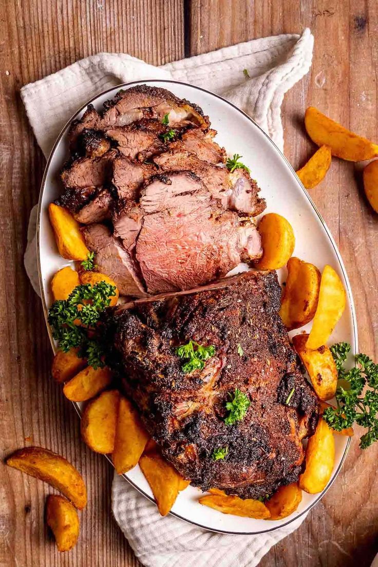 a white plate topped with meat and potatoes on top of a wooden table next to a fork