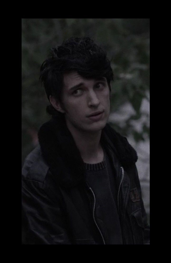 the young man is wearing a black jacket and standing in front of some trees with his eyes closed