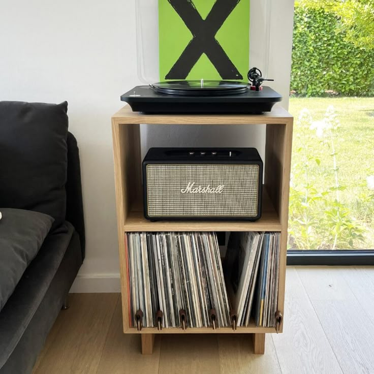 a record player sitting on top of a wooden shelf next to a couch and window