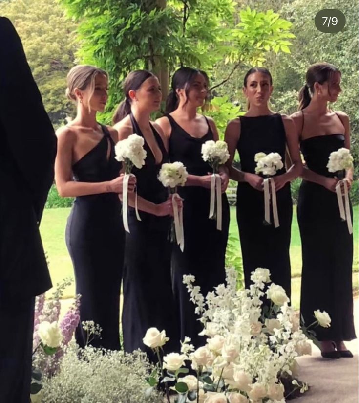 a group of women standing next to each other in front of flowers and greenery