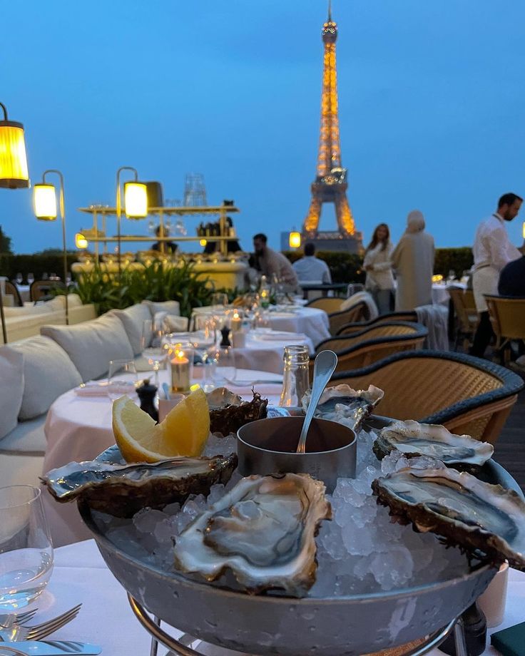 a table with oysters, lemon wedges and wine glasses on it in front of the eiffel tower