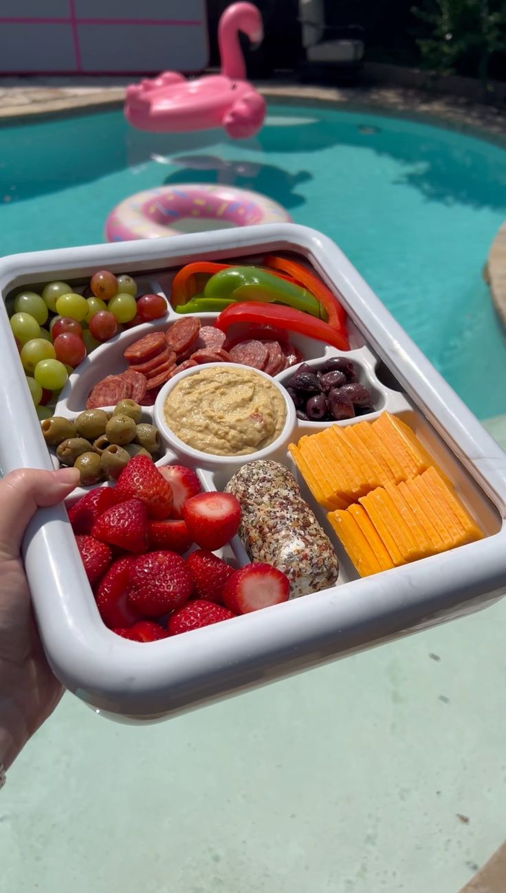 a person holding a tray full of food near a swimming pool with a pink flamingo in the background