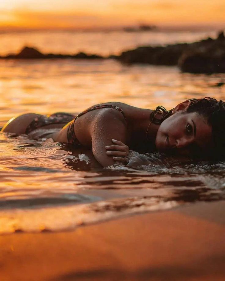 a woman laying on top of a body of water next to the ocean at sunset