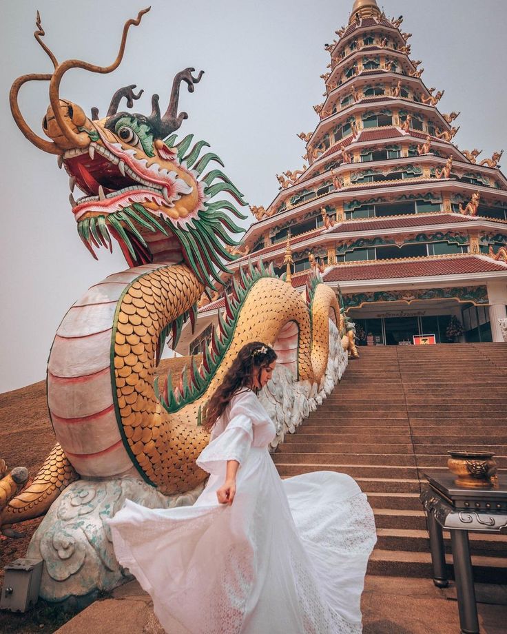 a woman in a white dress standing next to a dragon statue