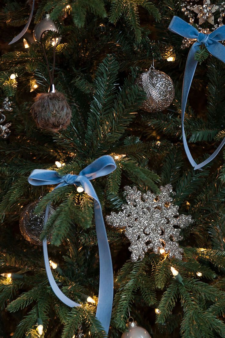 a christmas tree with ornaments on it and blue ribbon hanging from the top, in front of a white background