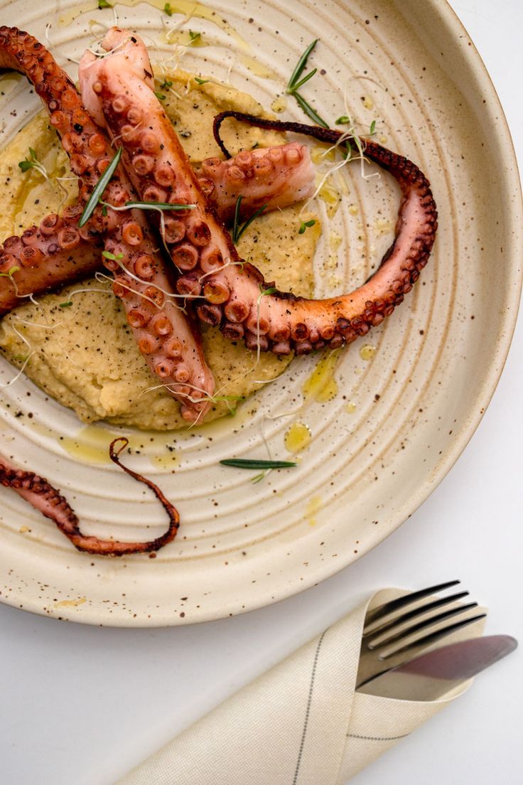 an octopus dish on a white plate next to a fork and knife