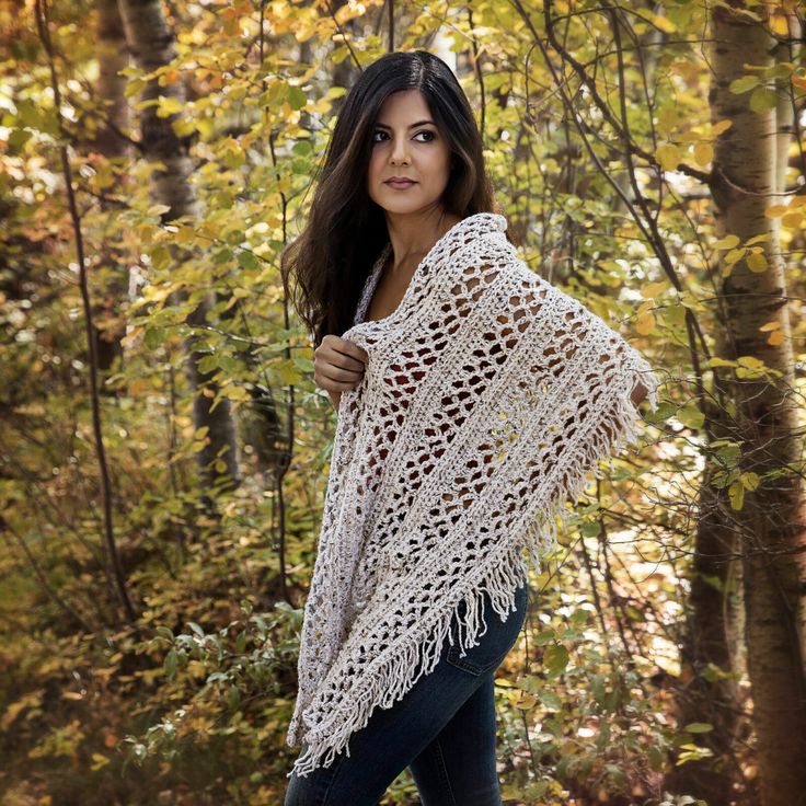 a woman standing in the woods wearing a white crocheted shawl with fringes