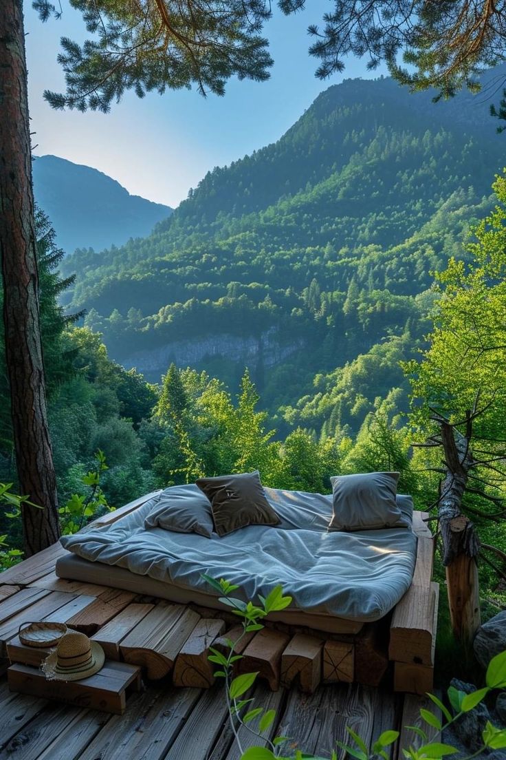 a bed made out of wood on top of a wooden platform in the woods with mountains in the background