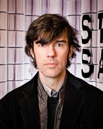 a man standing in front of a wall with stacks of books on it's sides