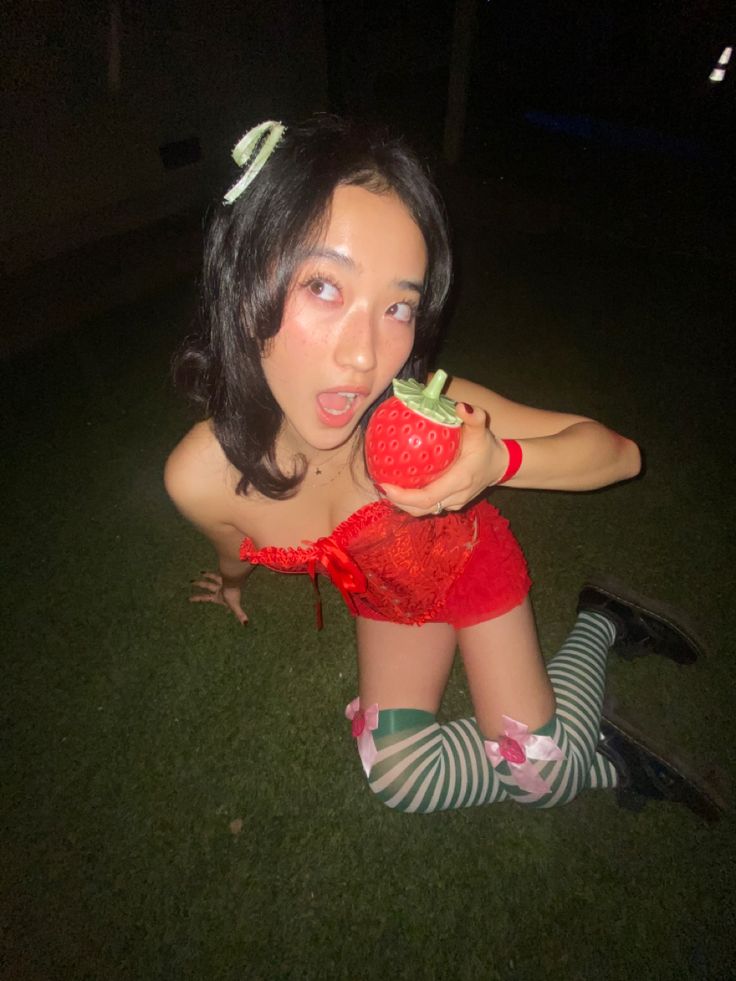 a woman sitting on the grass holding an apple in her hand and making a funny face