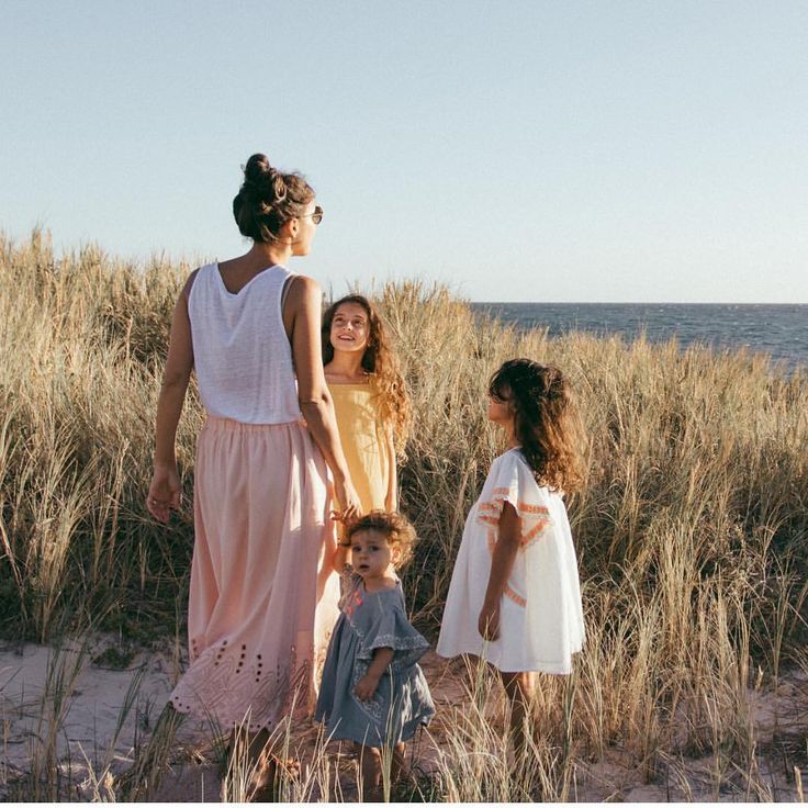 three women and two children standing in the sand at the beach looking out to sea