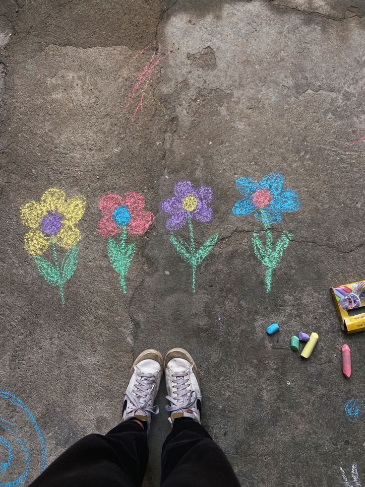 someone's feet standing in front of chalk flowers and crayons on the ground