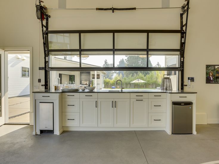 an empty kitchen with white cabinets and black counter tops in front of a large window