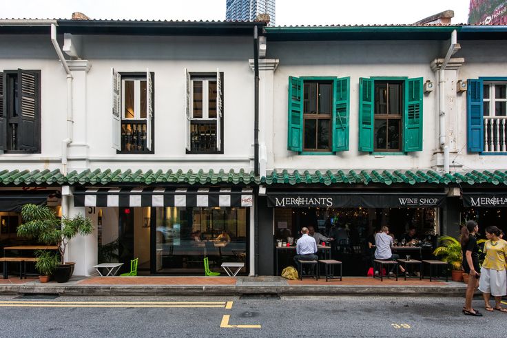 two people walking past an old building with green shutters on the front and side