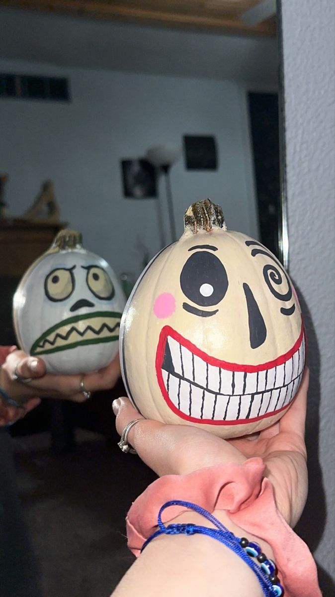 two pumpkins with faces painted on them being held by someone's hand in front of a mirror