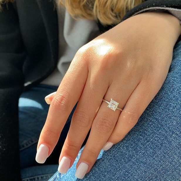 a woman's hand with a diamond ring on her left thumb and blue jeans