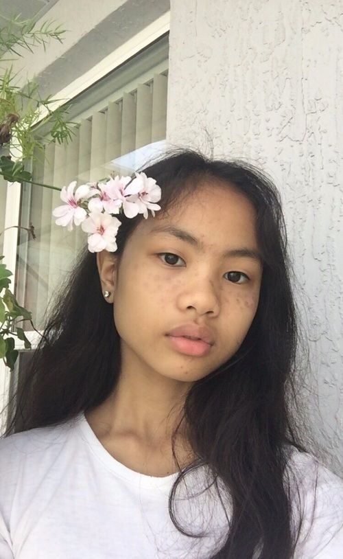 a girl with long hair wearing a flower in her hair and looking at the camera