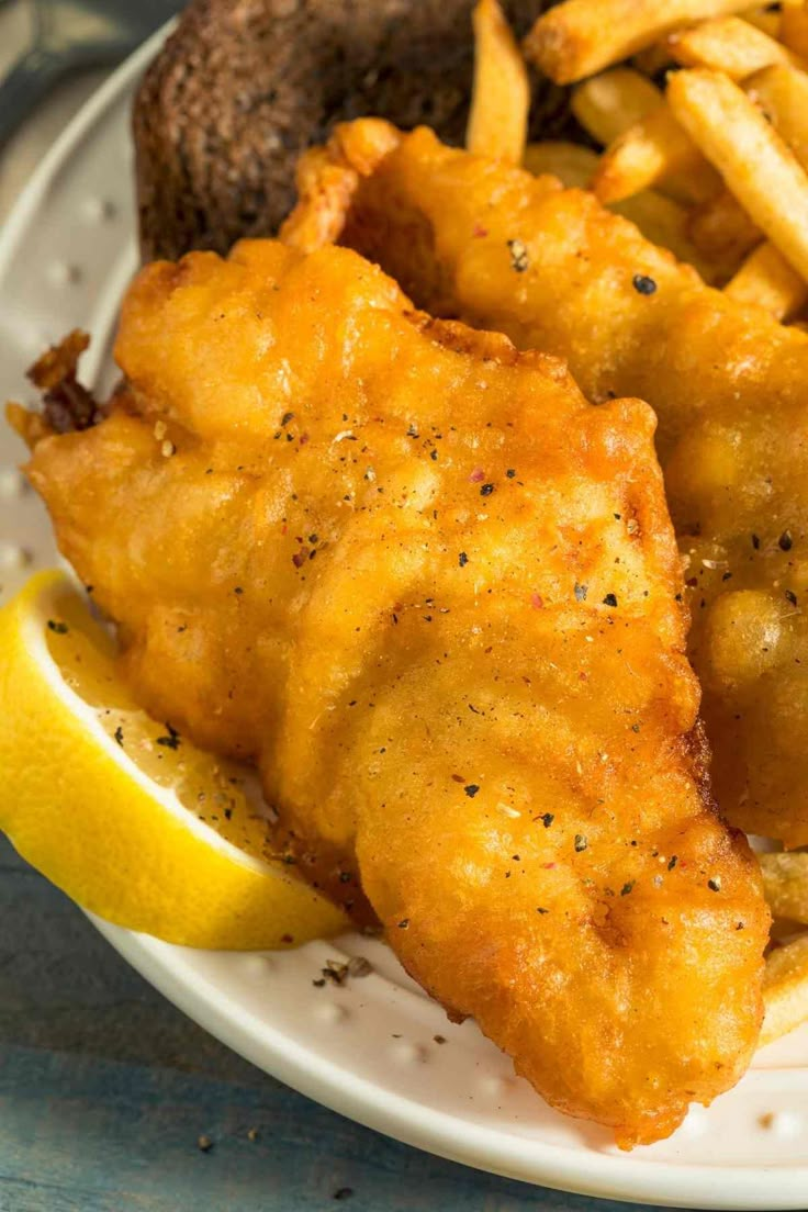 fried fish and fries on a plate with lemon wedges