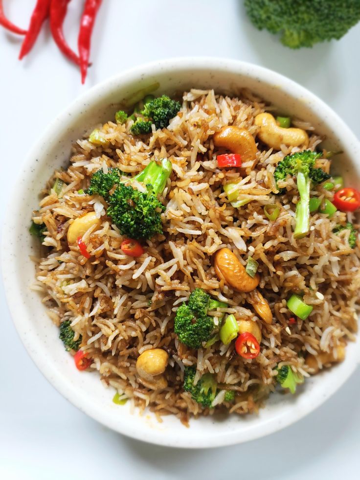 a white bowl filled with rice and broccoli on top of a table next to red peppers