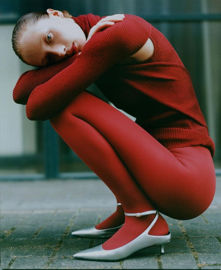 a woman in red is sitting on the ground with her legs crossed and hands behind her head