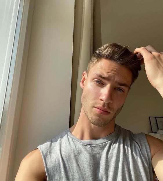 a young man is looking at the camera while holding his hair in one hand and wearing a gray tank top