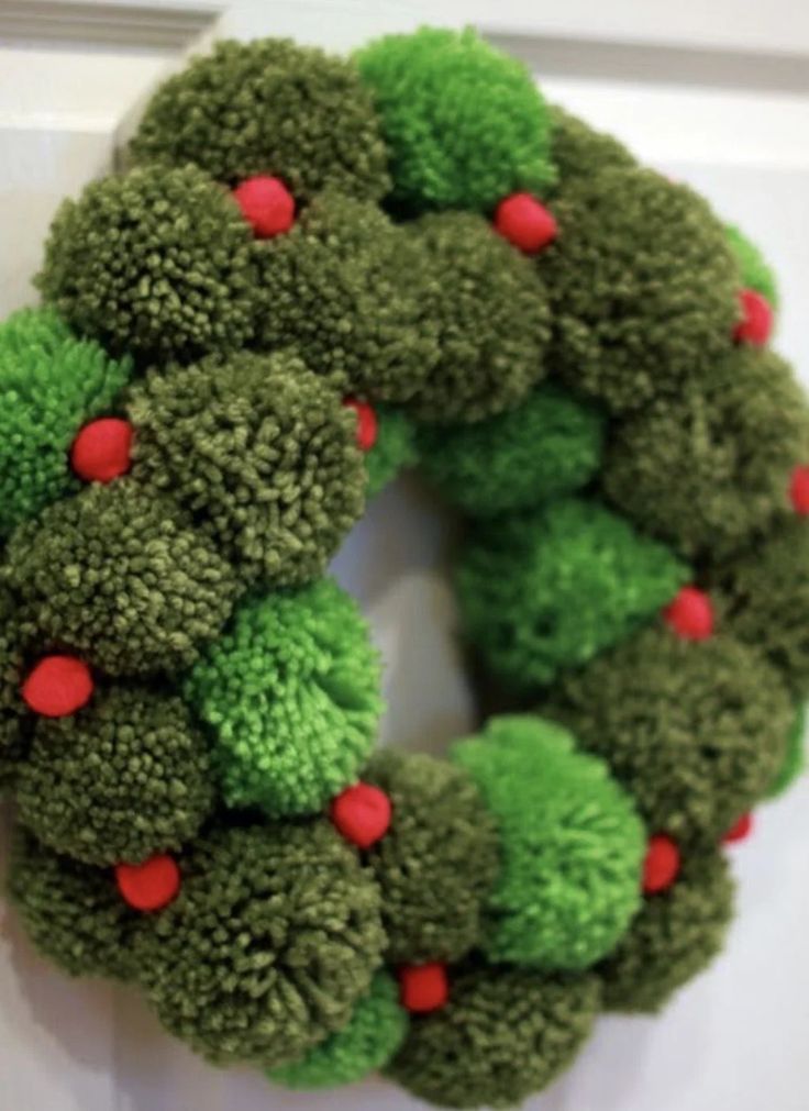 a green wreath with red berries hanging on the front door, decorated with pom - poms