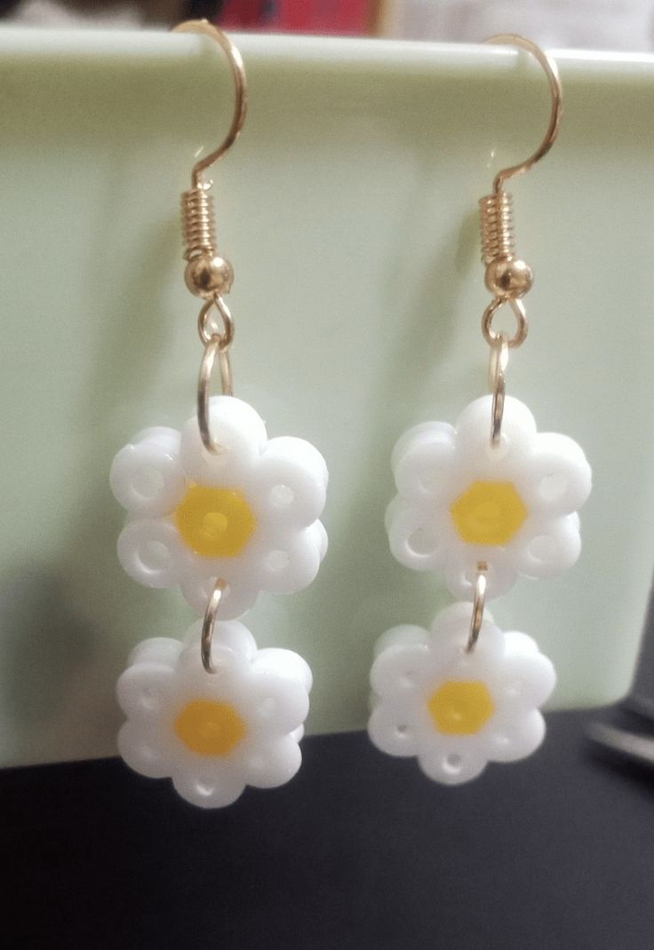 white and yellow flower dangles are hanging from gold earwires on a black surface