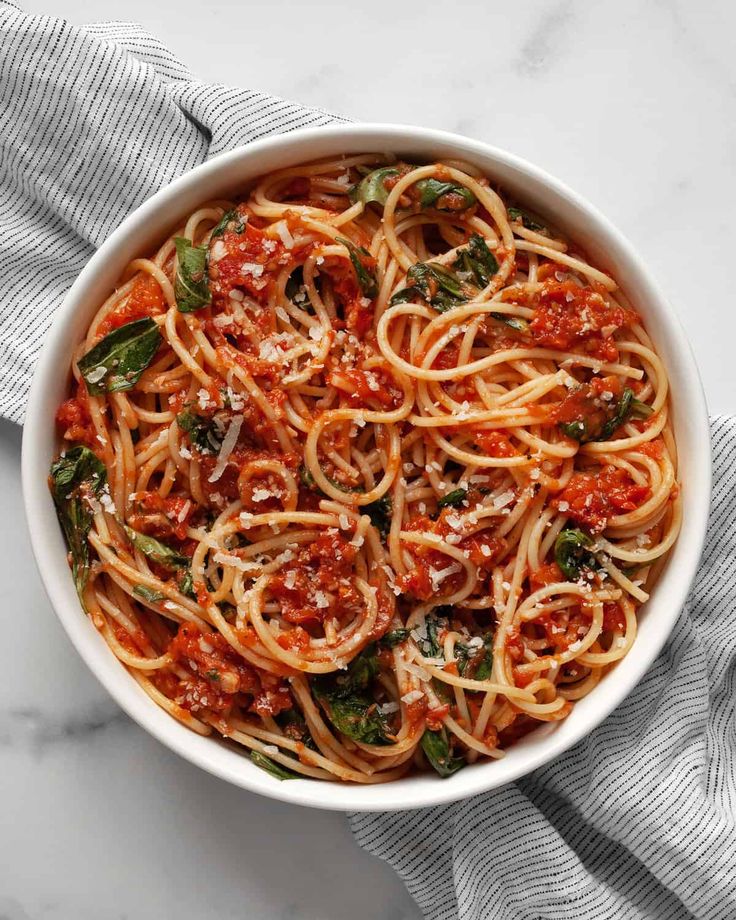 a white bowl filled with spaghetti and sauce on top of a marble countertop next to a gray towel